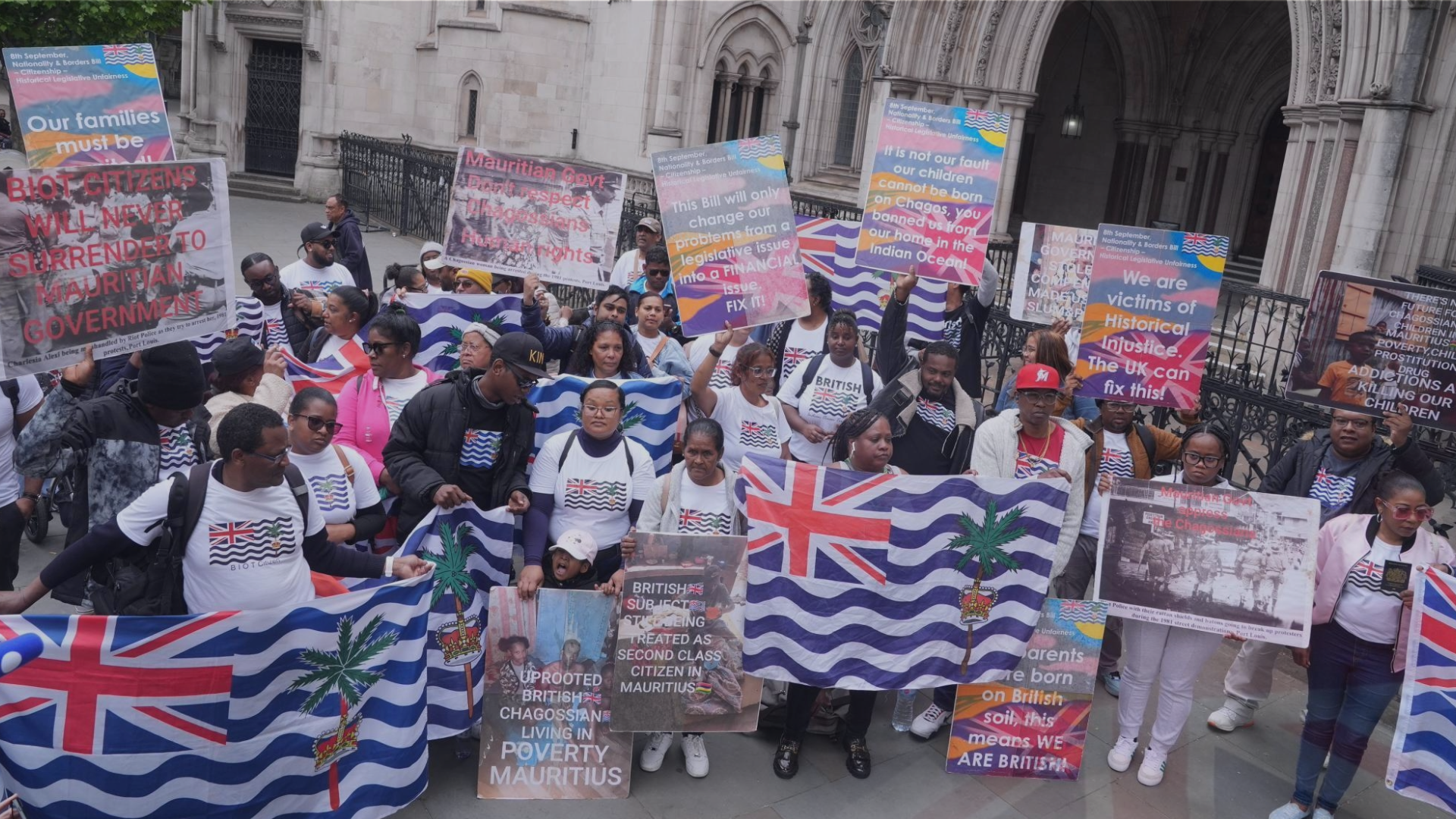 Protesters are gathered holding flags and placards, demanding justice for their land; Chagos Island.