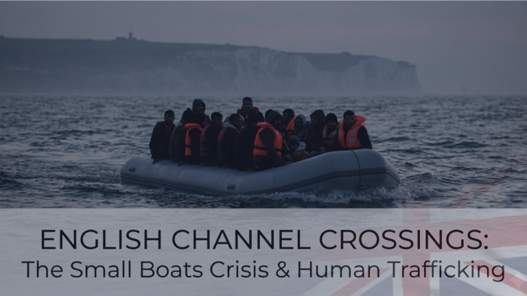 An extremely overcrowded grey inflatable dinghy, packed tightly with dozens of migrants, many wearing orange life vests, navigates dark, choppy waters with a prominent white cliff formation under a dramatic, overcast grey sky in the background.
